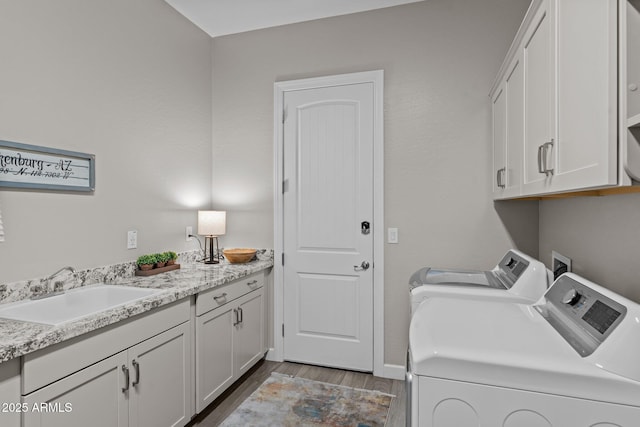 clothes washing area with cabinet space, baseboards, wood finished floors, washing machine and clothes dryer, and a sink