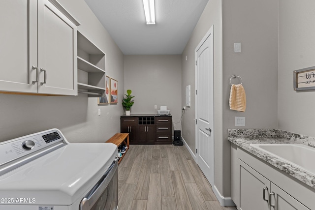 laundry room featuring washer / clothes dryer, cabinet space, a sink, light wood-type flooring, and baseboards