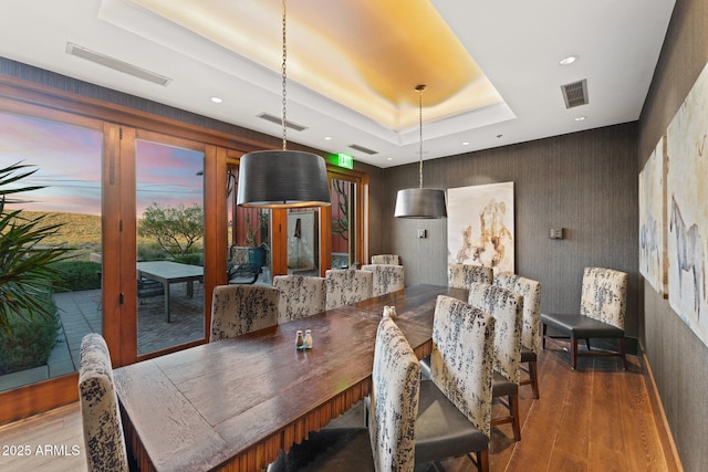 dining space featuring visible vents, a raised ceiling, and wood finished floors