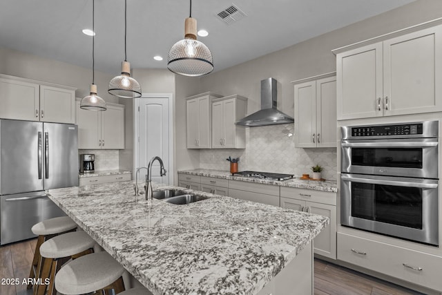 kitchen featuring dark wood-style flooring, stainless steel appliances, a kitchen bar, a sink, and wall chimney exhaust hood