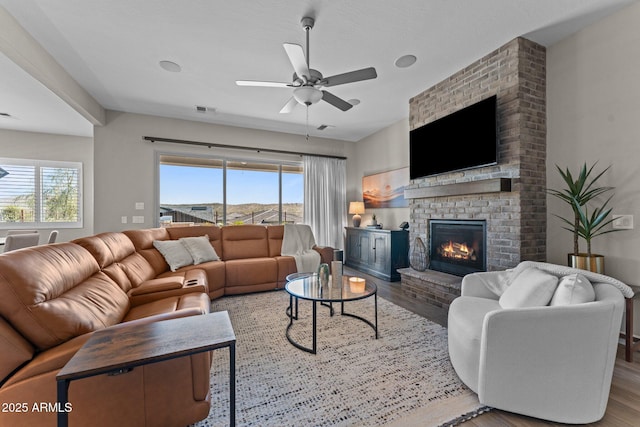 living room featuring a ceiling fan, a brick fireplace, visible vents, and wood finished floors