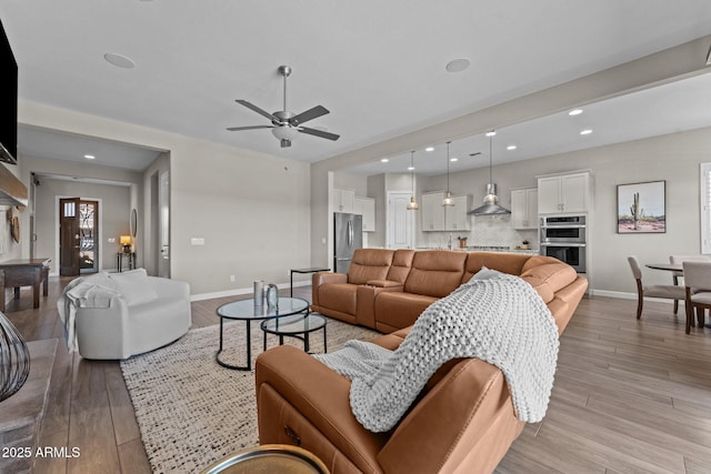 living area with baseboards, ceiling fan, recessed lighting, and light wood-style floors