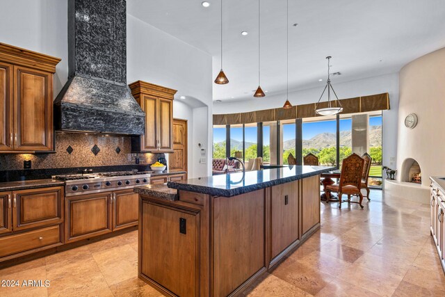 kitchen with tasteful backsplash, custom range hood, stainless steel gas cooktop, a kitchen island with sink, and decorative light fixtures