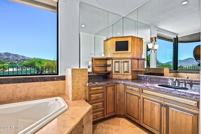 bathroom with a mountain view, vanity, a relaxing tiled tub, and a wealth of natural light