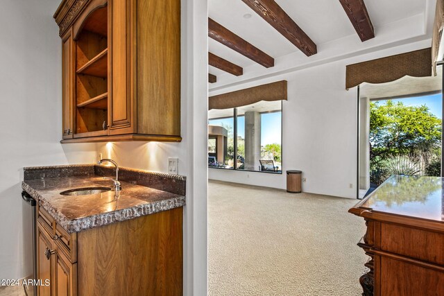 kitchen featuring beam ceiling, carpet floors, dark stone countertops, and sink