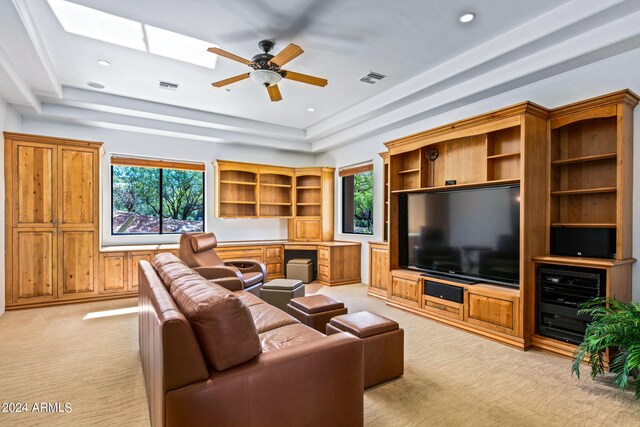 carpeted living room featuring a skylight, a tray ceiling, and ceiling fan