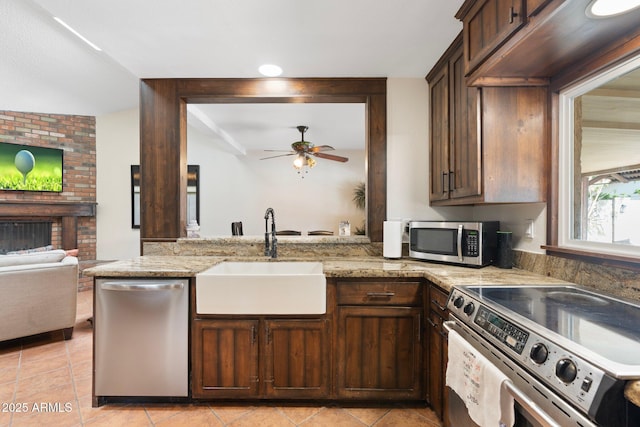 kitchen featuring light stone counters, a fireplace, a sink, stainless steel appliances, and dark brown cabinetry