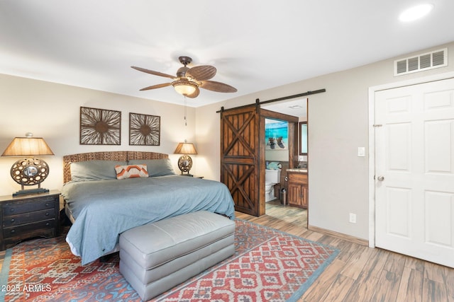 bedroom with light wood finished floors, visible vents, baseboards, a barn door, and ensuite bathroom