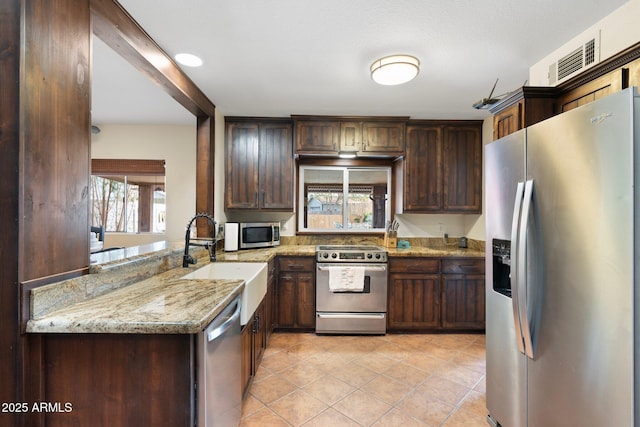 kitchen with light tile patterned floors, light stone counters, a sink, stainless steel appliances, and dark brown cabinets