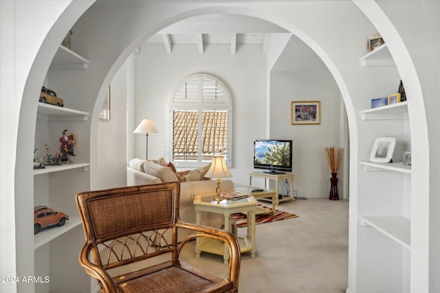 living area featuring built in shelves, beamed ceiling, and carpet floors