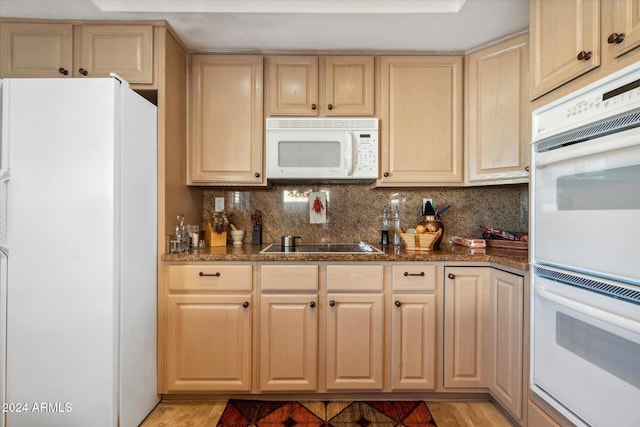 kitchen with light brown cabinetry, white appliances, dark stone counters, and backsplash