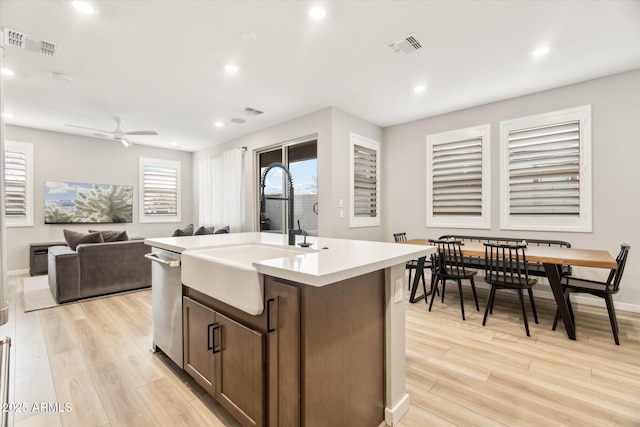 kitchen featuring sink, stainless steel dishwasher, a kitchen island with sink, and light wood-type flooring