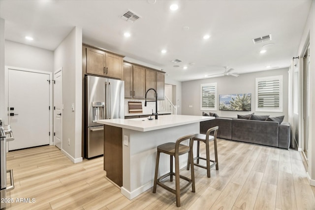 kitchen featuring high end refrigerator, a kitchen breakfast bar, light hardwood / wood-style floors, and a center island with sink