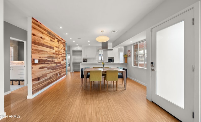 dining space featuring light wood-type flooring and wooden walls