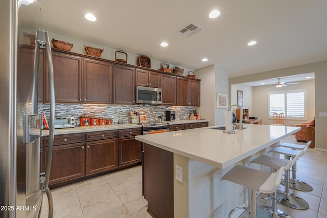 kitchen with appliances with stainless steel finishes, a breakfast bar area, decorative backsplash, sink, and a kitchen island with sink