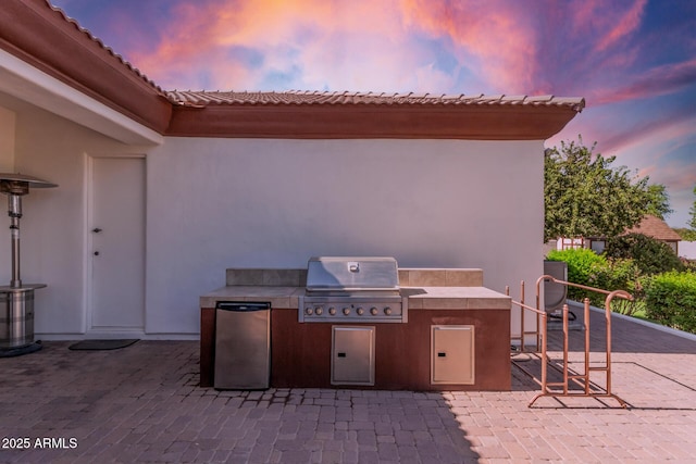 patio terrace at dusk featuring exterior kitchen and grilling area