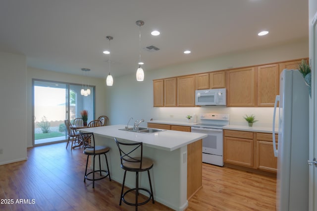 kitchen with light hardwood / wood-style floors, pendant lighting, sink, white appliances, and a kitchen island with sink