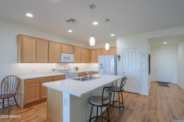 kitchen with pendant lighting, a breakfast bar, sink, white appliances, and an island with sink