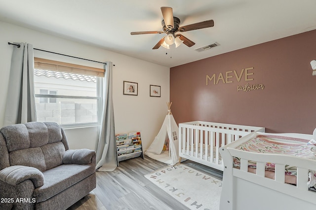 bedroom featuring ceiling fan, visible vents, a crib, and wood finished floors