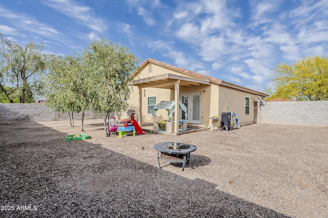 rear view of property with stucco siding, a fenced backyard, and an outdoor fire pit