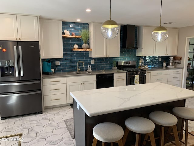 kitchen with wall chimney range hood, hanging light fixtures, sink, light stone countertops, and appliances with stainless steel finishes