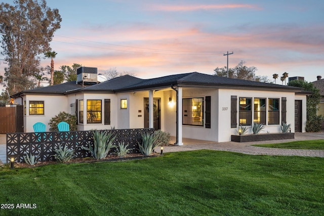 back house at dusk with central AC and a lawn