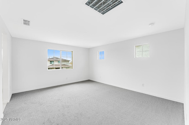 carpeted spare room featuring plenty of natural light, baseboards, and visible vents