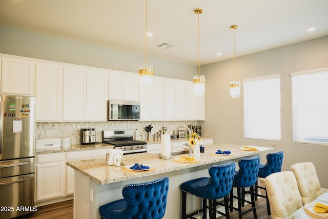 kitchen with an island with sink, appliances with stainless steel finishes, a breakfast bar area, and pendant lighting