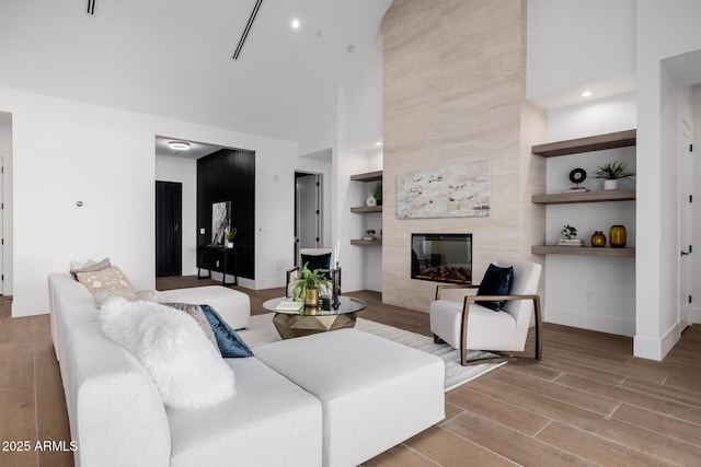 living room featuring baseboards, a premium fireplace, a high ceiling, light wood-type flooring, and built in shelves