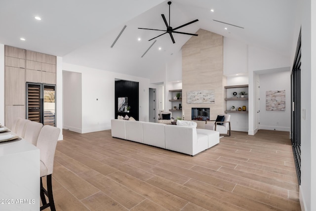 living area featuring light wood-style flooring, a fireplace, high vaulted ceiling, and baseboards