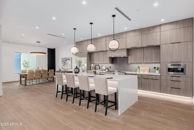 kitchen featuring light countertops, hanging light fixtures, light wood-style floors, modern cabinets, and a large island with sink