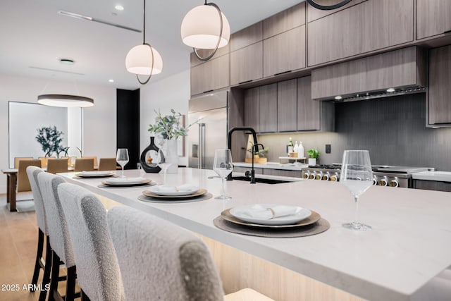 kitchen featuring pendant lighting, light countertops, stainless steel built in fridge, modern cabinets, and a kitchen breakfast bar