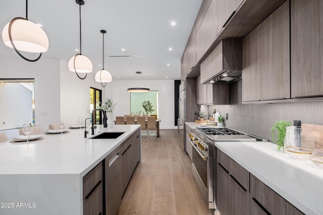 kitchen featuring modern cabinets, appliances with stainless steel finishes, hanging light fixtures, a sink, and backsplash