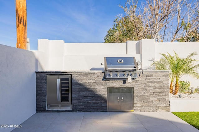 view of patio featuring a grill, fence, beverage cooler, and exterior kitchen