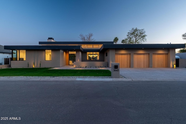 view of front facade with an attached garage, a front lawn, stucco siding, a chimney, and driveway