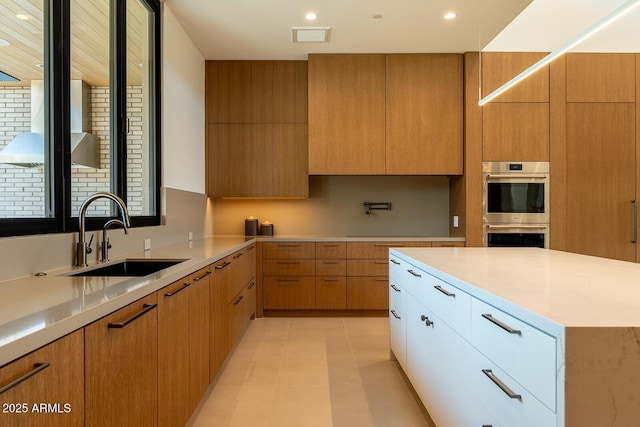 kitchen featuring stainless steel double oven, modern cabinets, light countertops, and a sink