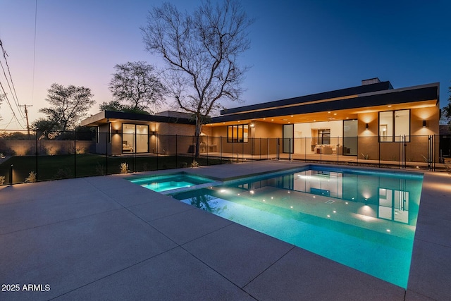 pool at dusk featuring a patio area, a pool with connected hot tub, and fence