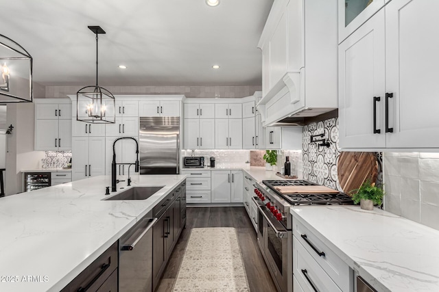 kitchen featuring decorative light fixtures, light stone countertops, high end appliances, white cabinets, and sink