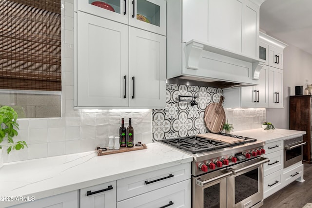 kitchen with white cabinets, light stone countertops, premium range hood, and stainless steel appliances