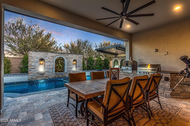 patio terrace at dusk featuring a grill, an outdoor kitchen, a fenced in pool, ceiling fan, and pool water feature