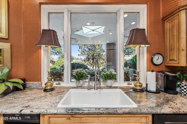 kitchen with stone countertops, a skylight, a sink, and wallpapered walls