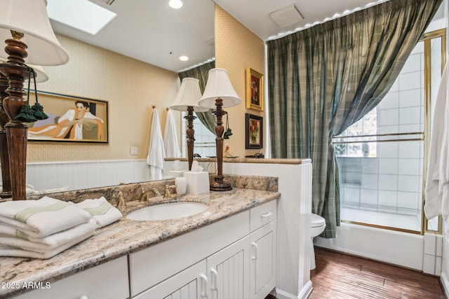 bathroom featuring a skylight, wood finished floors, vanity, and wallpapered walls