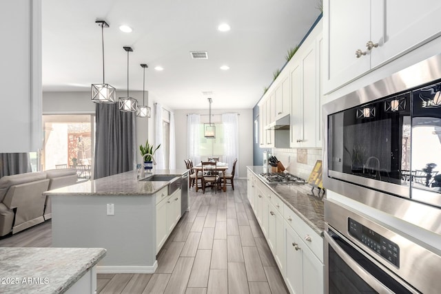 kitchen featuring under cabinet range hood, decorative backsplash, white cabinets, and stainless steel gas cooktop