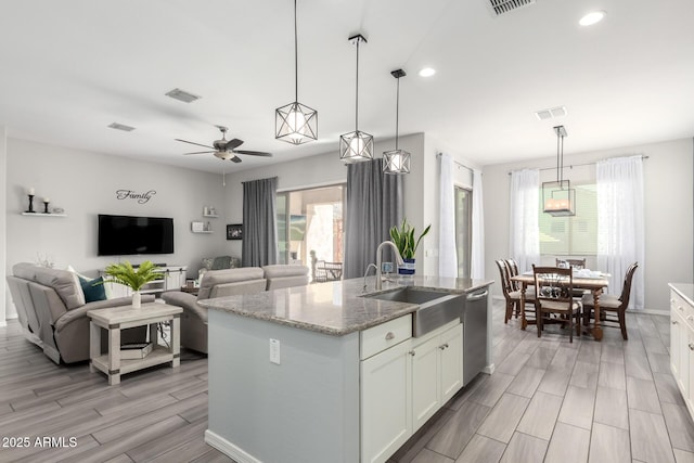 kitchen featuring wood finish floors, light stone countertops, dishwasher, white cabinets, and a sink