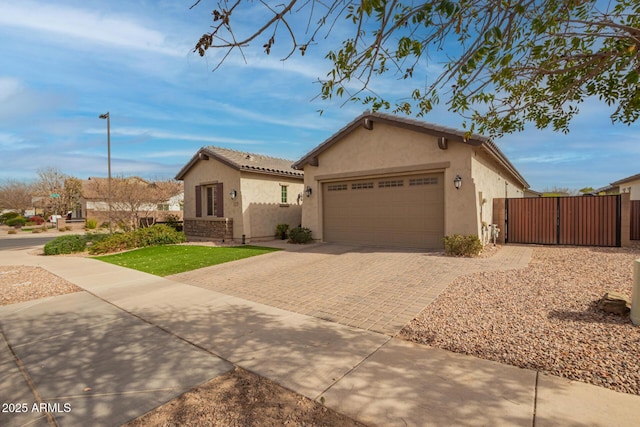 view of front facade with a gate, fence, stucco siding, a garage, and decorative driveway