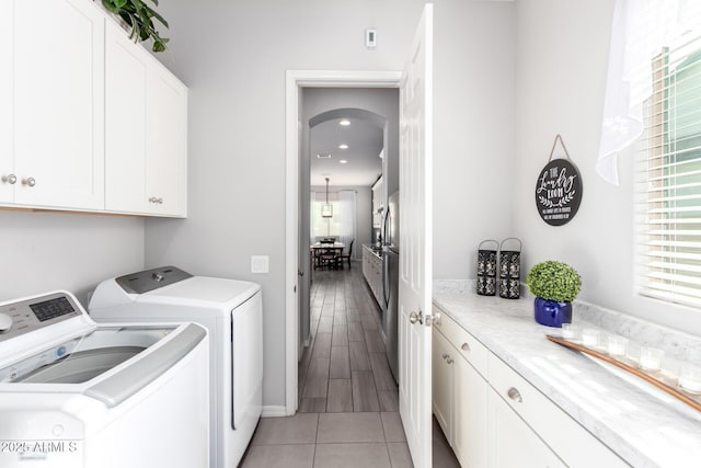 clothes washing area featuring cabinet space, plenty of natural light, washing machine and dryer, and arched walkways