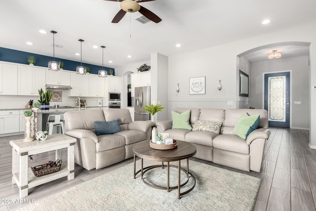 living room with wood finish floors, visible vents, a ceiling fan, recessed lighting, and arched walkways