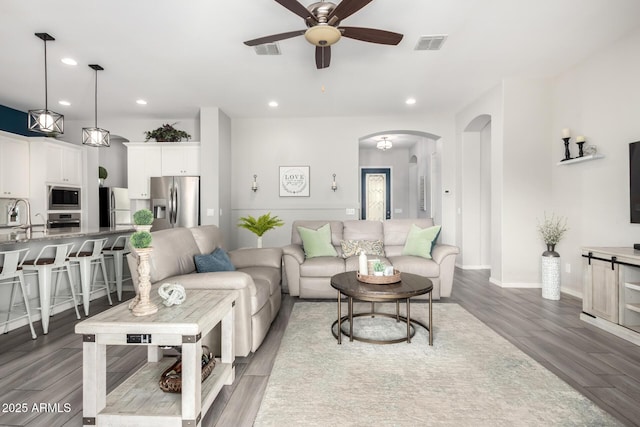 living area featuring arched walkways, visible vents, a ceiling fan, and wood finished floors