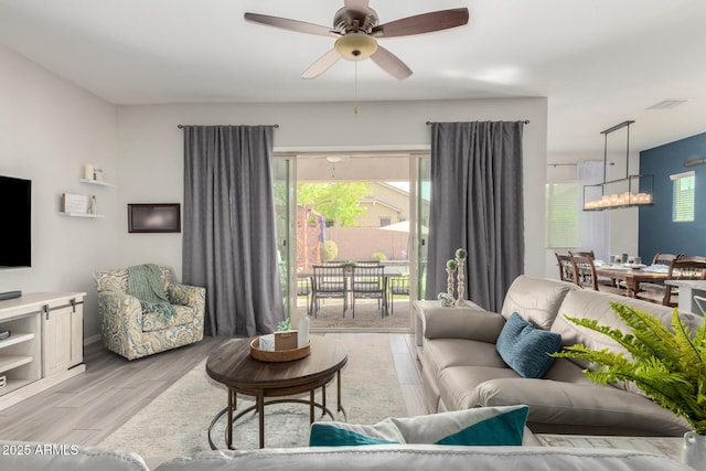 living room with light wood-style flooring and ceiling fan with notable chandelier