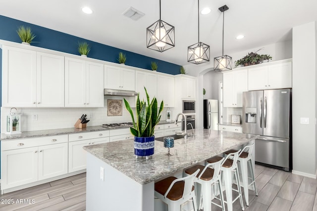 kitchen with tasteful backsplash, under cabinet range hood, appliances with stainless steel finishes, white cabinetry, and a sink